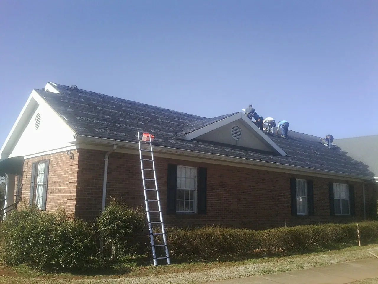 Crew tearing shingles off a brick ranch roof with a ladder set — Metal Roof Repair work by our crew in London