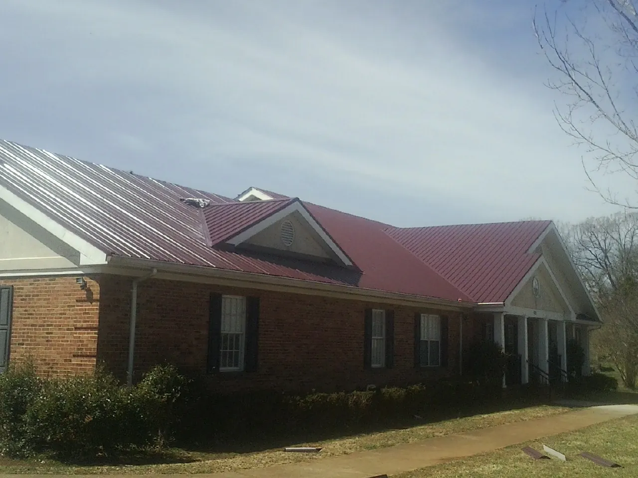 Red metal roof with gabled entries on a long brick building, from a Hail Damage Roof Repair job in London