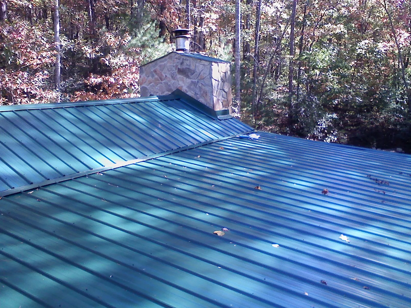 New green metal roof and stone chimney surrounded by autumn woods in London
