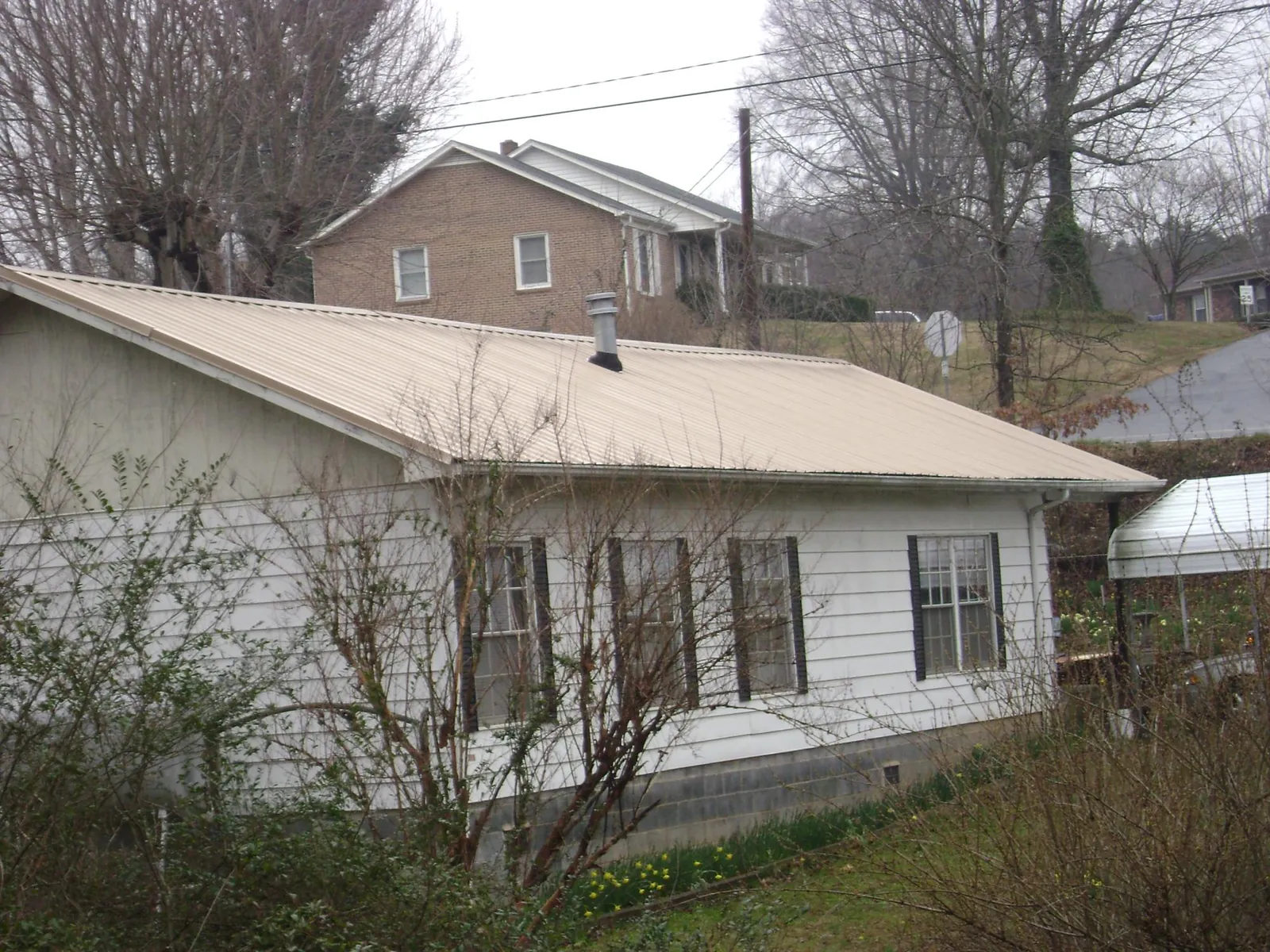 Tan metal roof on a white sided house set into a hillside — Commercial Roofing by Roofing Brothers in London